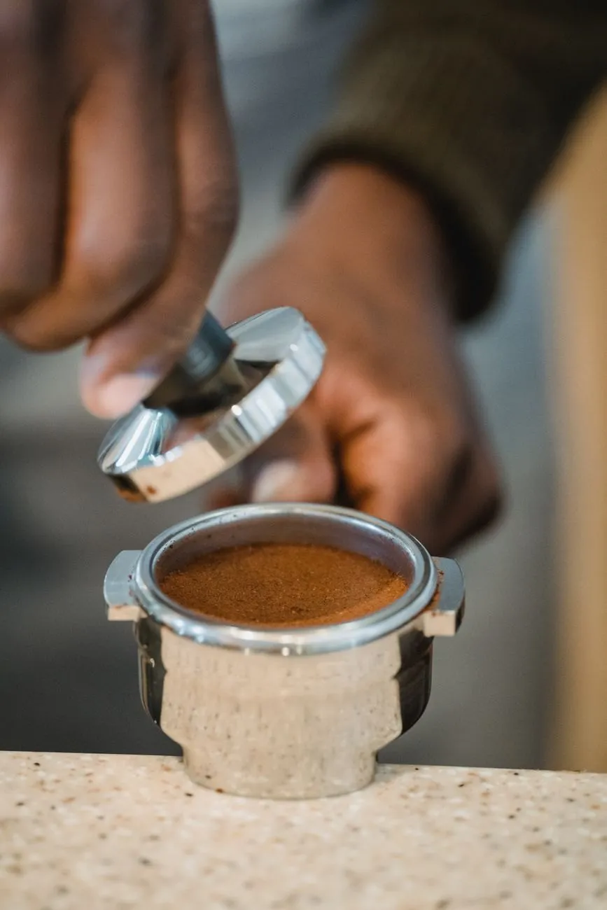 A barista lifting the tamper from a freshly tamped espresso basket